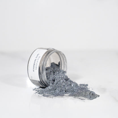 Pot transparent renversé avec de la poudre de mica gris scintillant sur un plan blanc