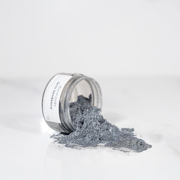 Pot transparent renversé avec de la poudre de mica gris scintillant sur un plan blanc