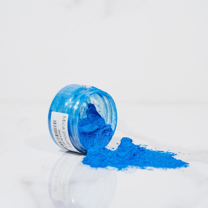 Pot transparent renversé avec de la poudre de mica bleu scintillant sur un plan blanc