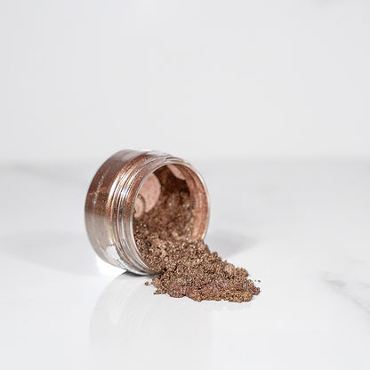 Pot transparent renversé avec de la poudre de mica brun mocca scintillant sur un plan blanc