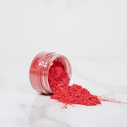 Pot transparent renversé avec de la poudre de mica rose/rouge scintillant sur un plan blanc