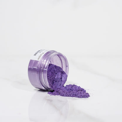 Pot transparent renversé avec de la poudre de mica violet scintillant sur un plan blanc
